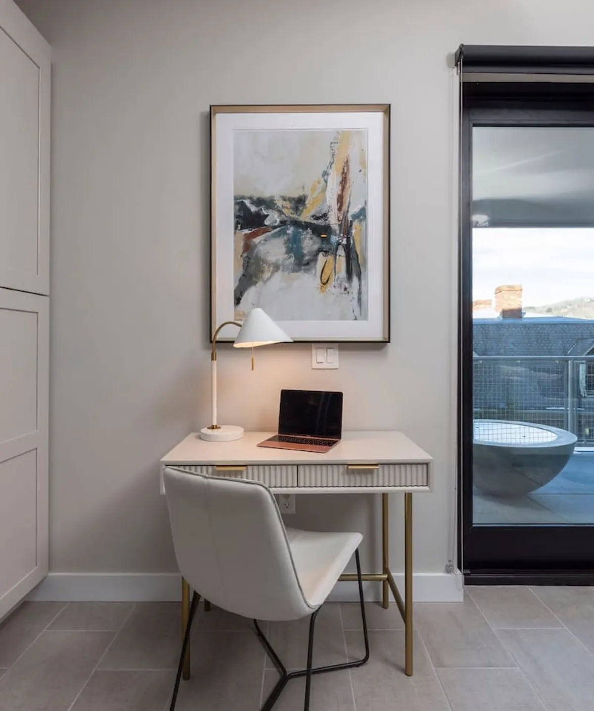 This image showcases a dedicated workspace with a desk, lamp, laptop, and abstract artwork, all bathed in natural light that suggests proximity to a balcony. The setup is ideal for both focused business tasks and creative brainstorming, embodying a balance between productivity and relaxation.