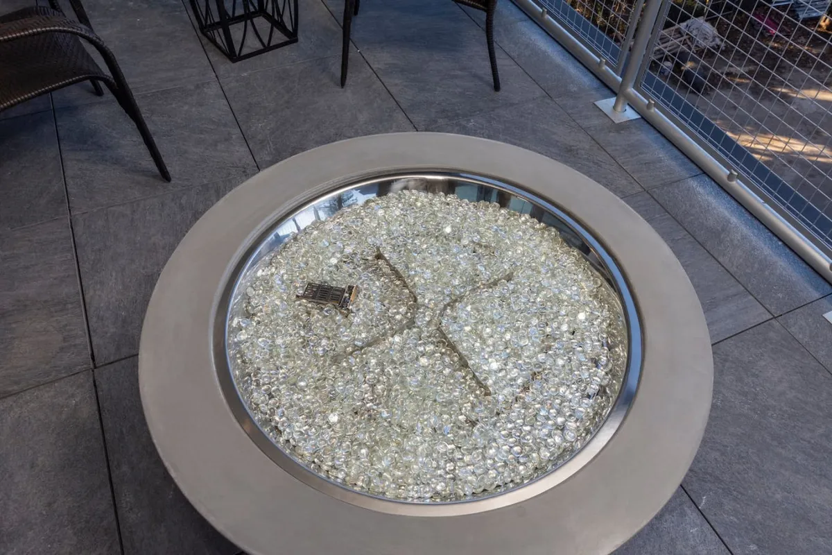 This image depicts a cozy fire pit with decorative stones and surrounding seating, suggesting an inviting outdoor space for relaxing or socializing. The setup hints at a balcony or terrace area that encourages guests to unwind in comfort, especially during evenings.
