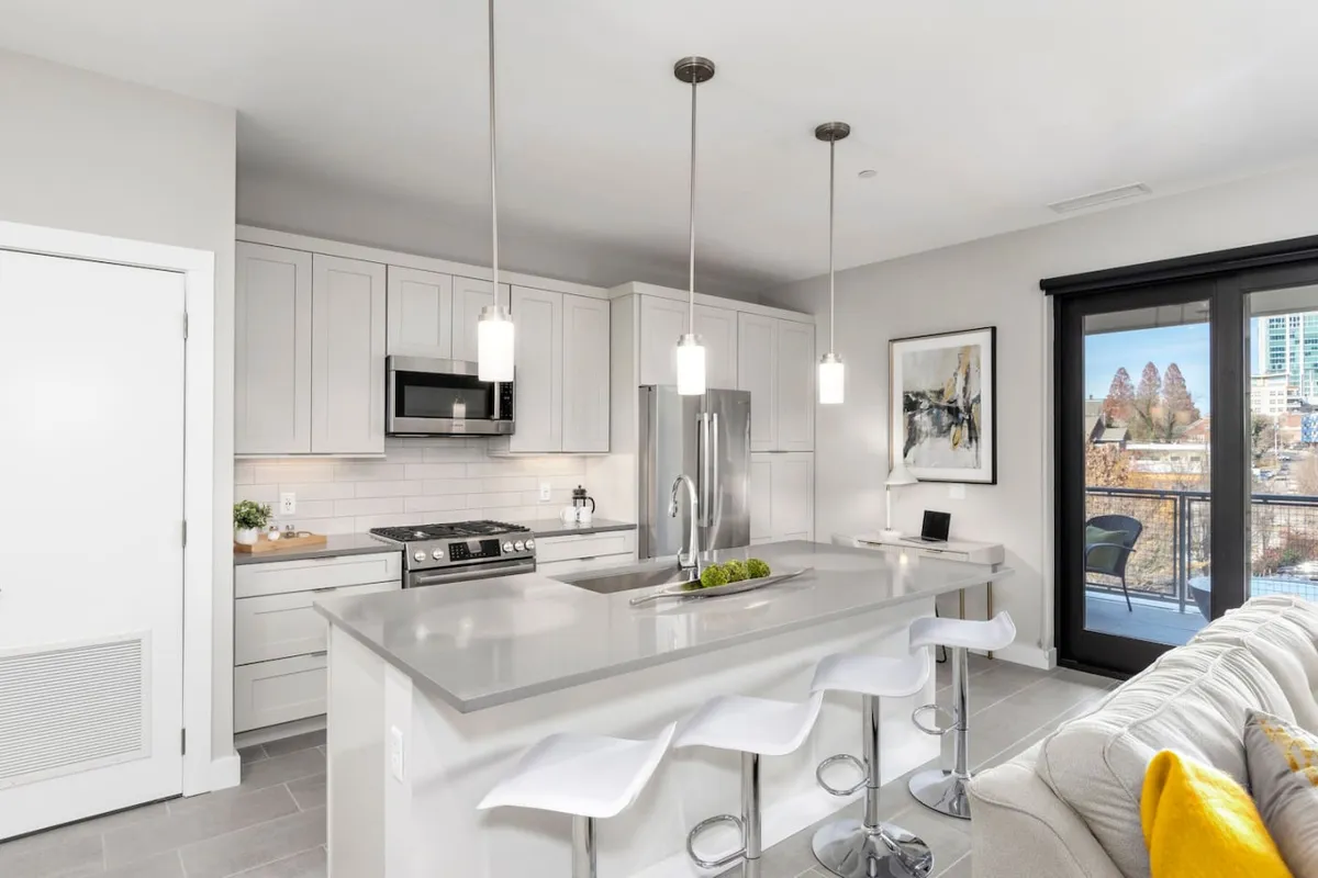 A modern kitchen featuring a large island, stainless steel appliances, expansive windows, and colorful wall art. The setup is ideal for entertaining, with open sightlines and ample space for group activities, reflecting the vibrancy of Asheville’s culinary and social scene.