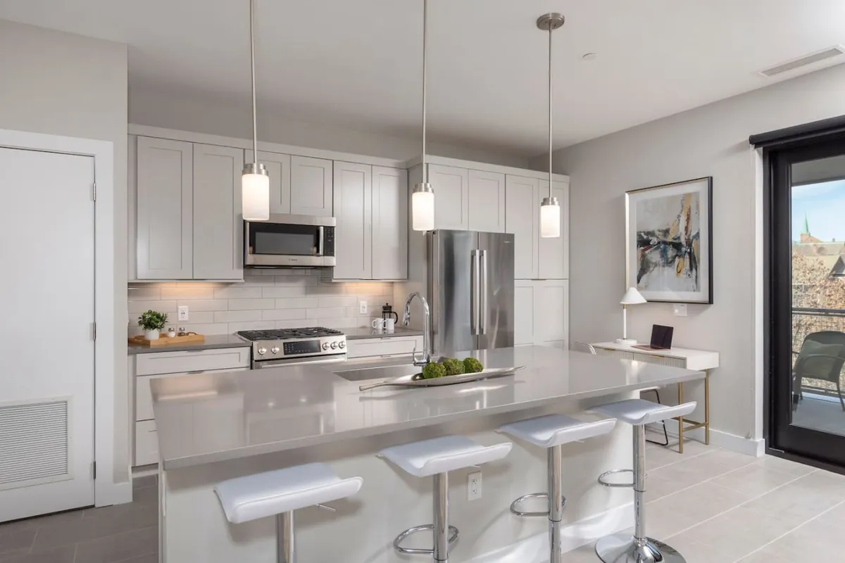 A contemporary kitchen highlighted by a central island with bar stools, stainless steel appliances, pendant lighting, and a view towards a balcony—blending style and function for cooking and casual dining.