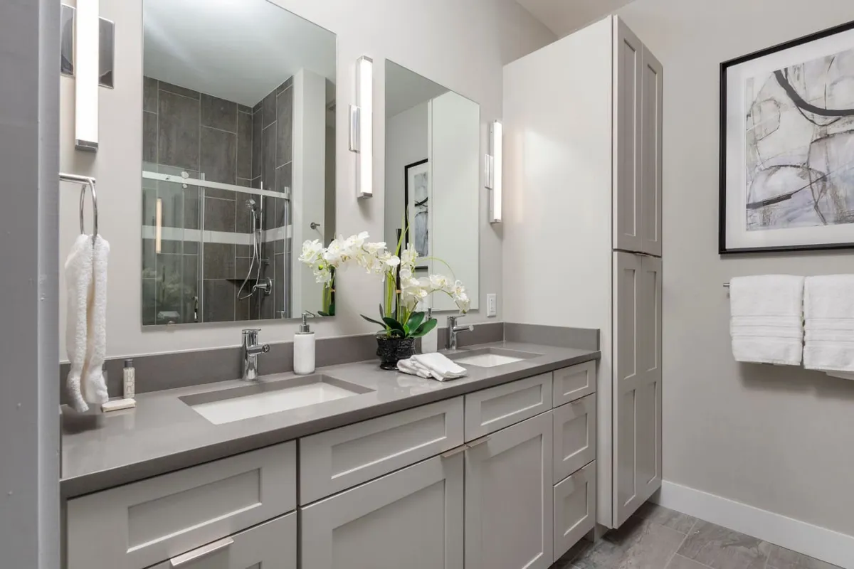 A modern bathroom featuring double vanity sinks, elegant mirrors, an orchid arrangement, and framed artwork. The space feels serene and spa-like, ideal for morning routines or relaxing self-care rituals.